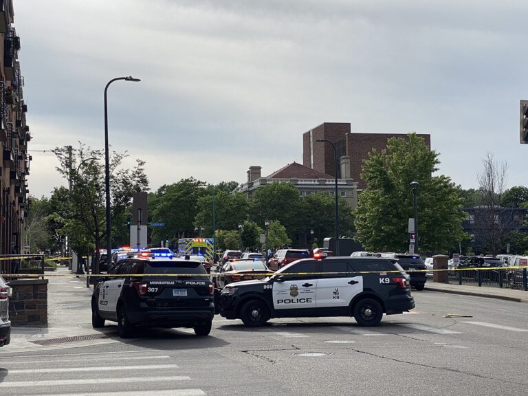 Escena de investigación policial en la calle. Un coche de policía y otros vehículos están presentes.