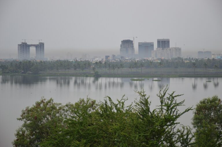 Vista de un horizonte urbano brumoso sobre un cuerpo de agua, indicando contaminación atmosférica.