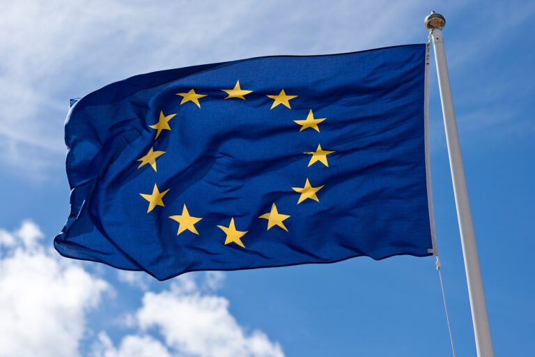 Bandera de la Unión Europea ondeando bajo un cielo azul con nubes.