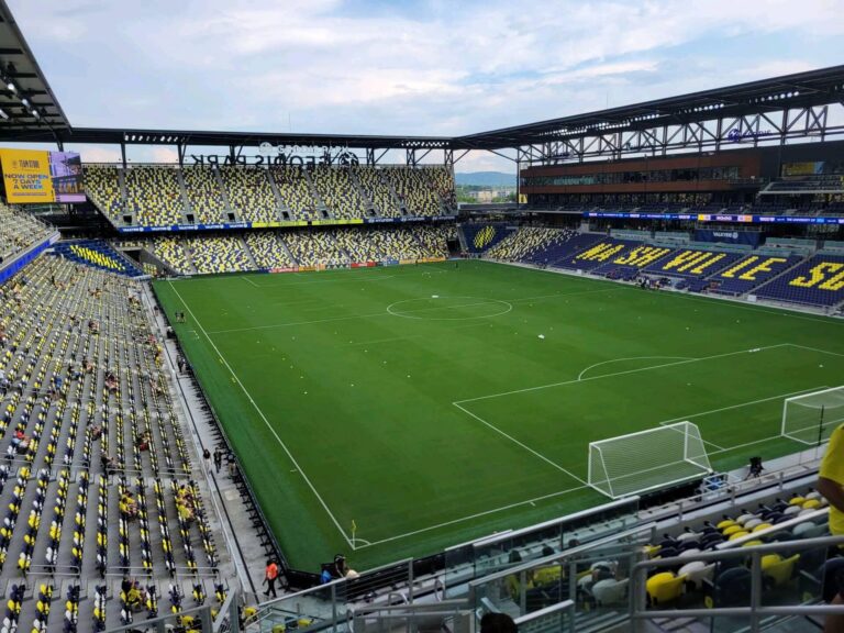 Vista panorámica de un estadio de fútbol profesional con gradas llenas y césped bien cuidado.