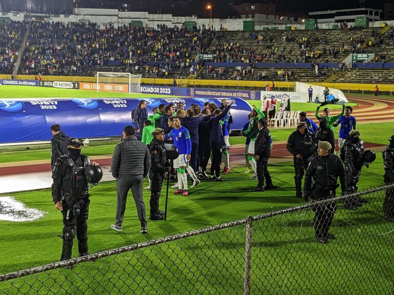 Jugadores y personal en el campo de un estadio lleno durante un evento de fútbol.