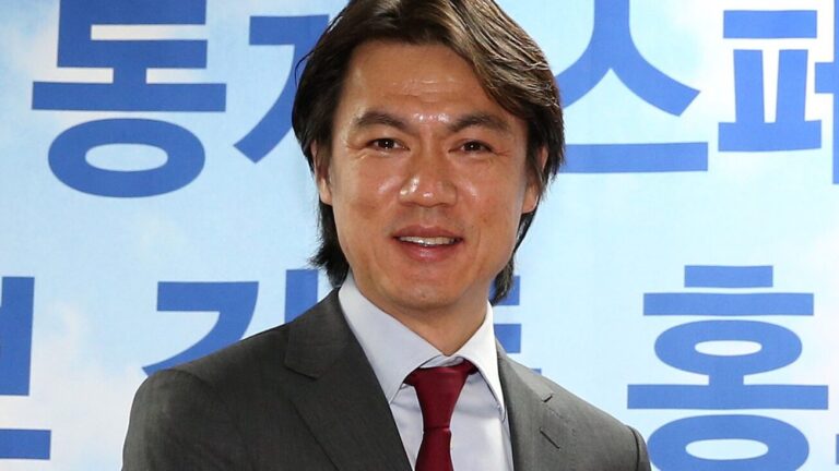 Hong Myung-bo, en traje, sonriendo y sosteniendo un trofeo o premio.