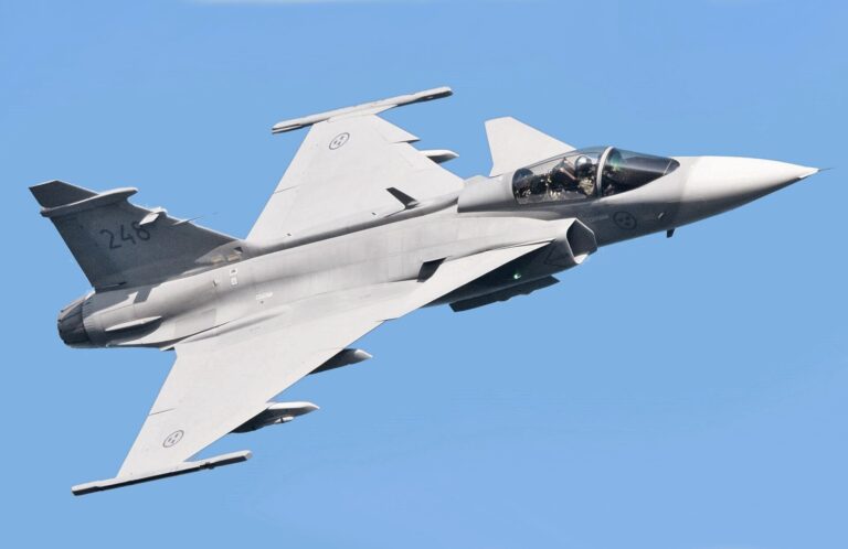 Un caza Saab Gripen en vuelo contra un cielo azul despejado.