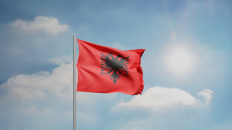 Bandera de Albania ondeando contra un cielo azul con nubes.