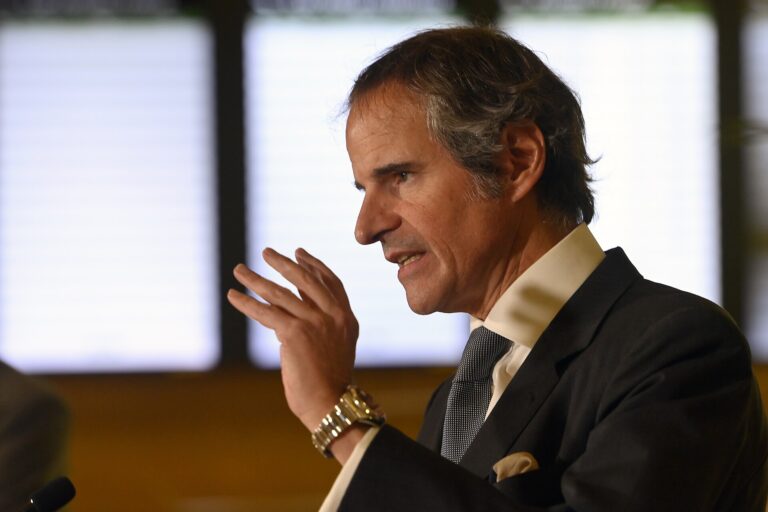 Hombre de mediana edad con traje oscuro hablando en un evento, gesticulando con ambas manos.