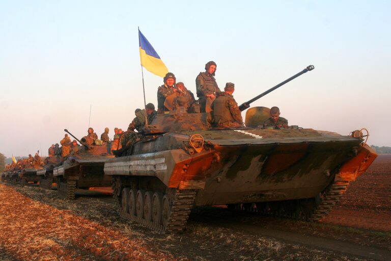 Tanque militar con soldados en el equipo, ondeando la bandera de Ucrania en un campo abierto.