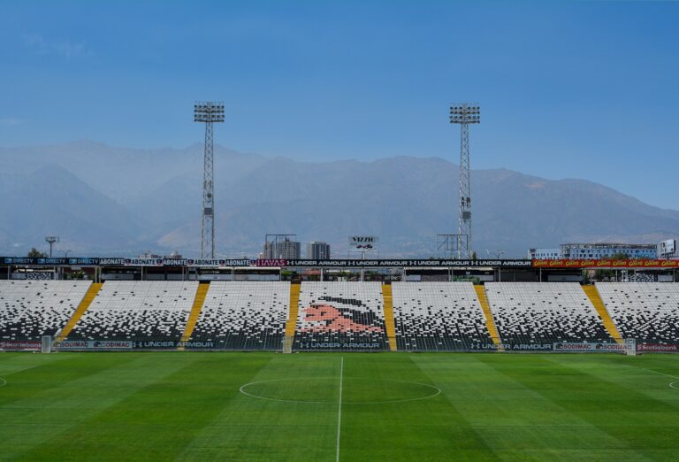 Vista de las gradas de un estadio de fútbol con montañas al fondo.