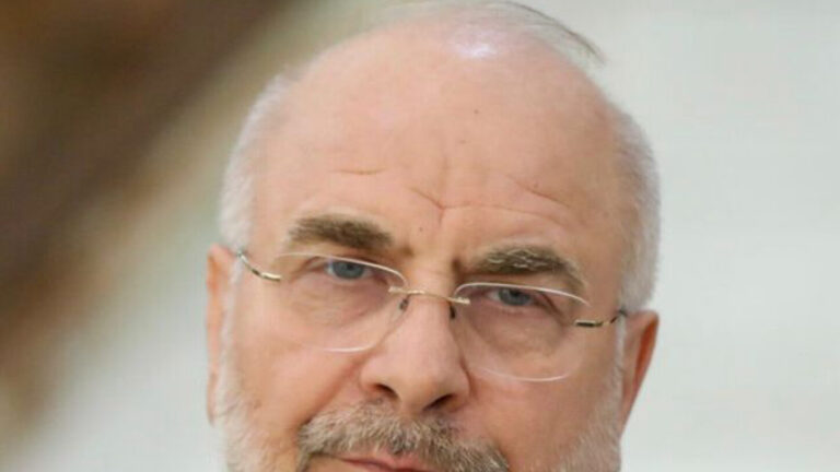 Retrato de un hombre mayor con barba, gafas y traje, mirando directamente a la cámara.