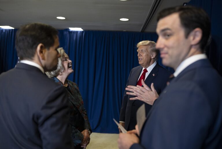 Donald Trump interactuando con otros hombres en un evento interior.