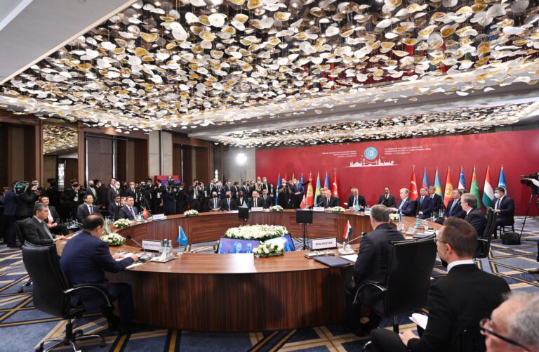 Sala de conferencias grande con muchos delegados sentados en mesas en forma de herradura.