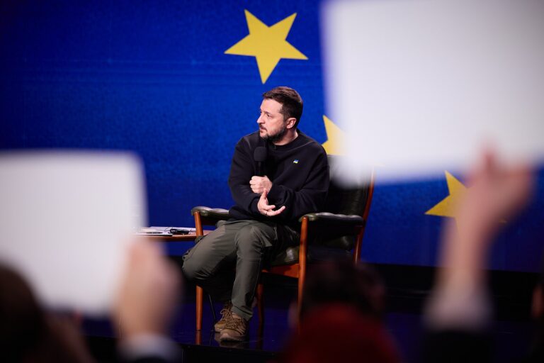 Volodymyr Zelenskyy hablando en una conferencia de prensa con fondo de estrellas doradas.