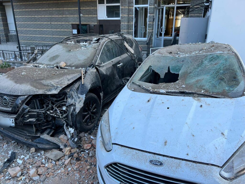 Dos coches dañados en una calle urbana, con restos y escombros alrededor.