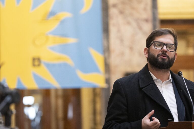 Gabriel Boric hablando en un evento, con una bandera chilena al fondo.