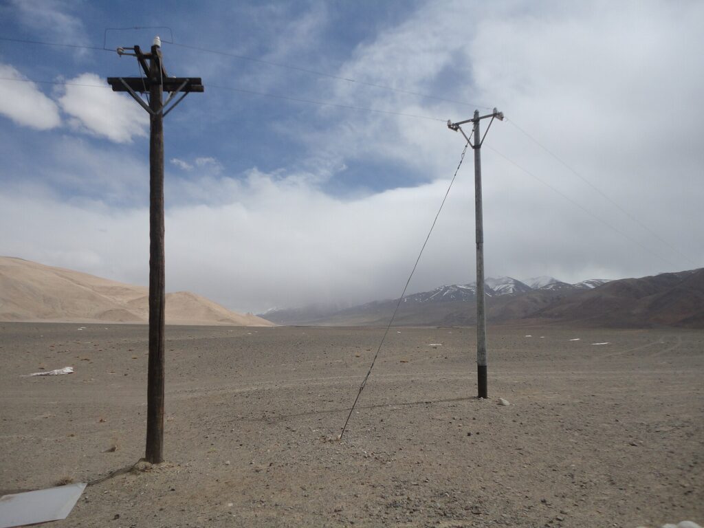 Paisaje fronterizo en el Himalaya, mostrando postes de electricidad en un terreno árido con montañas al fondo.