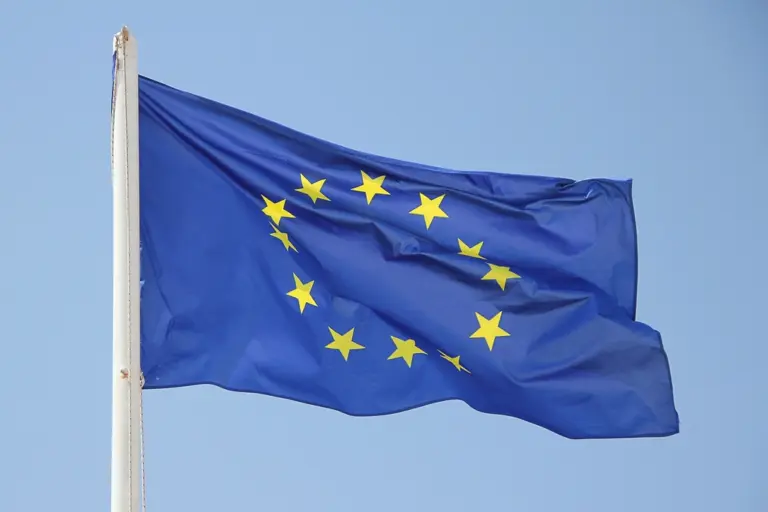 Bandera de la Unión Europea ondeando en un mástil contra un cielo azul claro.