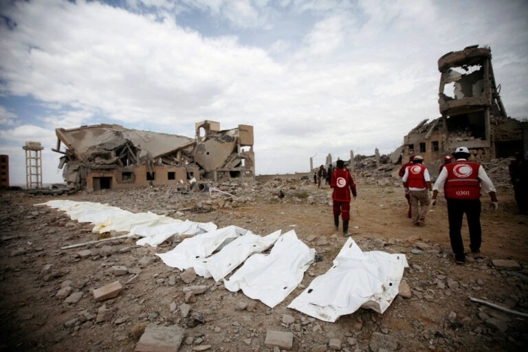 Ruinas de edificios después de los ataques aéreos en Yemen, con personas en el fondo.